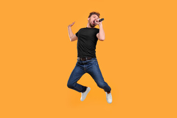 Fototapeta premium Handsome man with microphone singing and jumping on yellow background