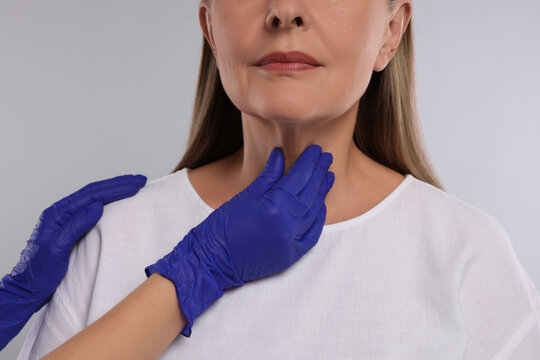 Endocrinologist examining thyroid gland of patient on light grey background, closeup