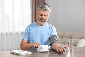 Man measuring blood pressure at table indoors