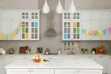 Wicker baskets with Easter eggs at white marble table and festive decor in kitchen