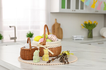 Wicker baskets with Easter eggs and willow twigs at white marble table in kitchen