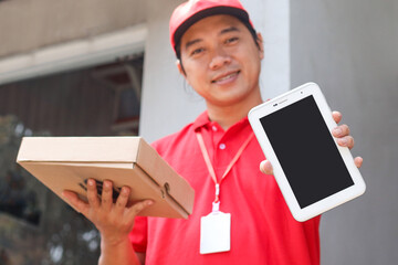 Deliveryman from pizza restaurant in red t-shirt and cap holding pizza box and showing copyspace screen of cell phone