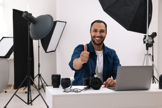 Young professional photographer with camera showing thumbs up in modern photo studio