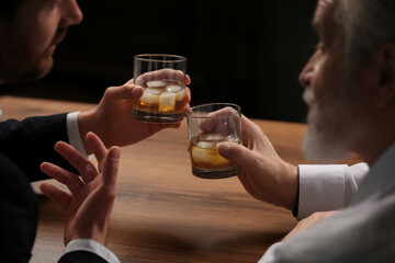 Men with glasses of whiskey talking at wooden table in bar