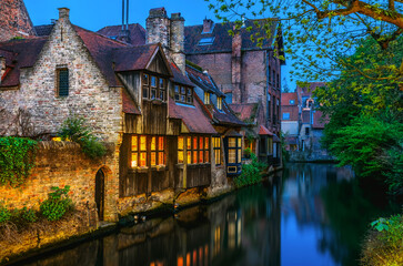 Medieval houses over canal in Bruges Belgium evening landscape panorama with vintage architecture blue sky and reflection water.