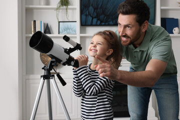 Little girl with his father looking at stars through telescope in room