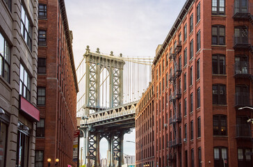 famous Manhattan Bridge between Manhattan and Brooklyn over East River seen from a narrow alley enclosed by two brick buildings on a sunny day, New York City