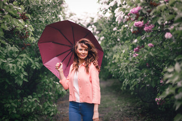 Happy girl with umbrella in park with Lilac that blooms