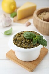Delicious pesto sauce in bowl and ingredients on white wooden table