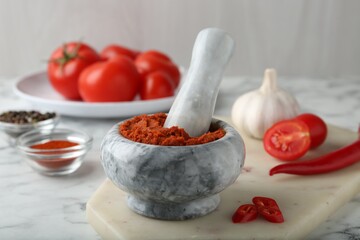 Red curry paste in mortar and ingredients on white marble table