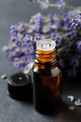 Bottle with essential oil near lavender on grey table, closeup
