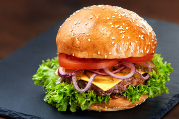 Hamburger on stone table with black background. Fastfood meal. Delicious and gourmet hamburger. Classic hamburger. Appetizing food. Hamburger with grilled meat, tomatos, cheese, onion and lettuce.