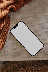 Phone with blank screen lying on the light couch or chair. Smart phone mock-up in neutral tones
