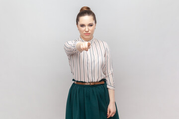 Portrait of serious strict bossy woman wearing striped shirt and green skirt standing pointing to...