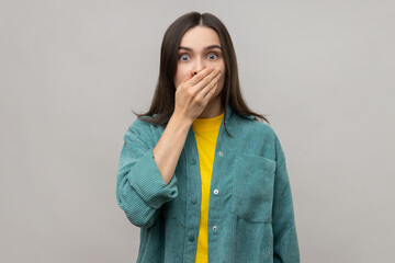 Portrait of scared shocked dark haired woman closing mouth with hand, afraid to say too much,...