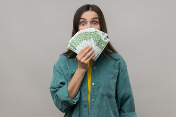 Amazed happy woman with dark hair hiding face behind fan of euro banknotes, interest-free cash...