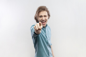 Portrait of overjoyed cheerful joyful young man standing pointing at camera, selecting you, smiling, expressing positive emotions, wearing blue shirt. Indoor studio shot isolated on gray background.