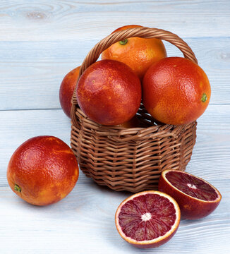 Ripe Blood Oranges Full Body and Two Halves in Wicker Basket closeup on Blue Wooden background