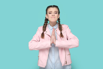 Portrait of hopeful teenager girl with braids wearing pink jacket standing keeps hand in praying...