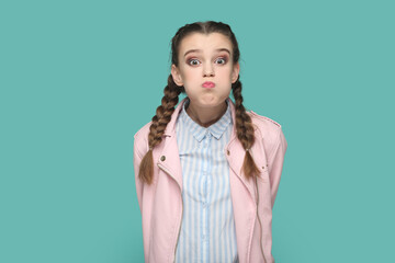 Portrait of funny teenager girl with braids wearing pink jacket blowing cheeks and puffing breath, has attractive look keeps silence with friends. Indoor studio shot isolated on green background. - obrazy, fototapety, plakaty