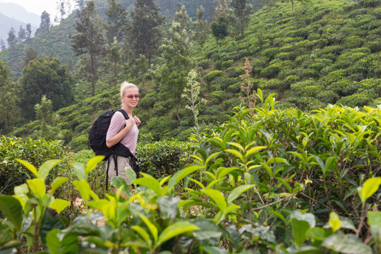 Active caucasian blonde woman enjoying fresh air and pristine nature while trekking among tea plantations near Ella, Sri Lanka. Backpacking outdoors tourist adventure.