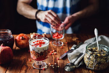 Obraz na płótnie Canvas Dessert with Pomegranate and Guy Prepare New Portion on Backdrop. Series on Prepare Healthy Dessert with Pomegranate, Granola, Cream and Jam