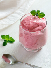 Healthy Strawberry or Raspberry Cream mousse in glass on a white wooden table with mint leaves and spoon. Delisious summer dessert. Top view, vertical