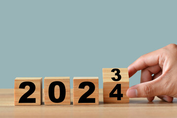Close up image of hand flipping wood block from 2023 to 2024. Merry Christmas and Happy New Year, blue background.2024 new year idea concept.