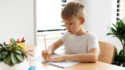 A cute boy makes a drawing with a ruler and pencil. Home lessons. Geometry and drawing.