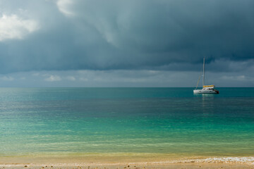 Fototapeta na wymiar A gloomy sky above the turquoise calm sea and a small white yacht