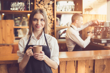 Professional barista. Young man in apron working at bar counter with coffee machine. Woman holding cup of coffee
