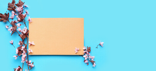 Blooming tree branches with pink flowers and blank greeting card on blue background. Banner for design