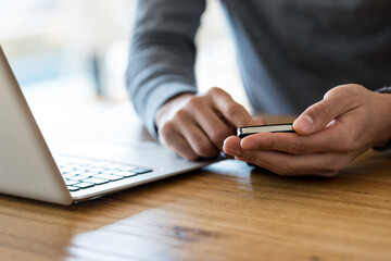 Obraz premium Close-up of unrecognizable man in grey sweater sitting at wooden table next to laptop and holding cell phone in both hands
