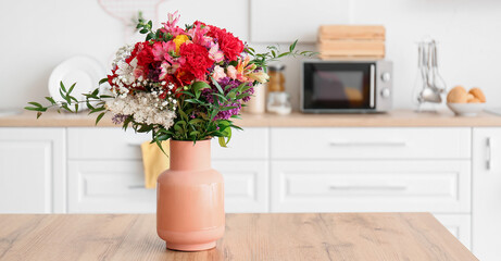 Vase with bouquet of beautiful flowers on table in kitchen