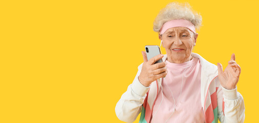 Sporty senior woman with earphones and mobile phone on yellow background with space for text