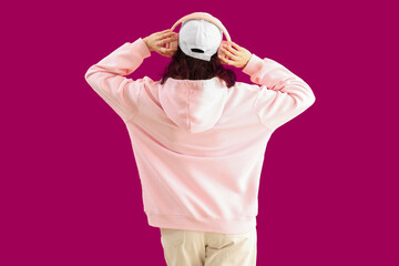 Young woman in headphones on pink background, back view