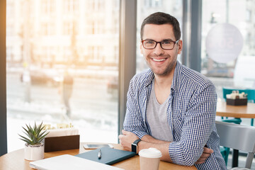 Coffee time. Handsome young man in cafe with big window. Man with cup of coffee to go. Man with glasses looking at camera and smiling