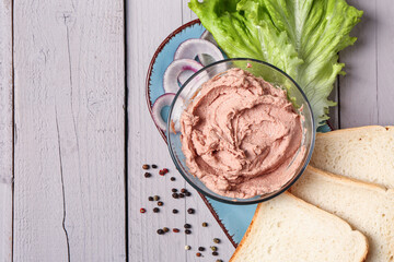 Bowl of delicious pate, bread and lettuce on light wooden background