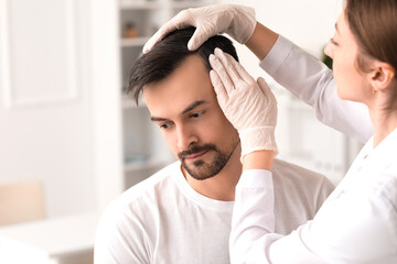 Doctor examining young man's hair in clinic, closeup
