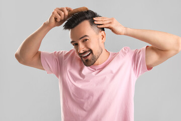 Handsome man combing hair on grey background