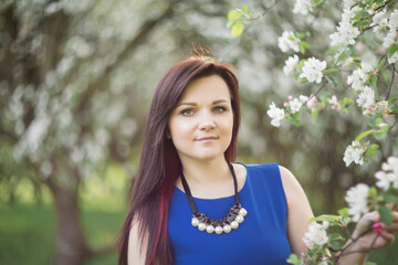 beautiful young brunette woman standing near the blossoming apple tree on a warm spring day.