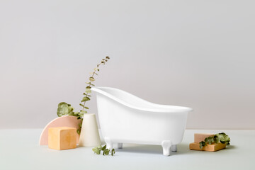 Small bathtub, plaster decor and eucalyptus branches on light background