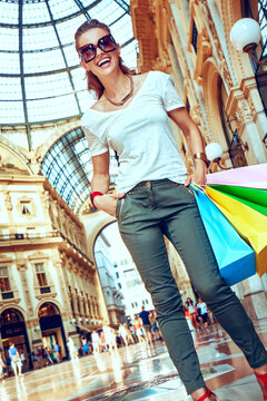 Discover most unexpected trends in Milan. Full length portrait of smiling fashion woman in eyeglasses with colorful shopping bags in Galleria Vittorio Emanuele II