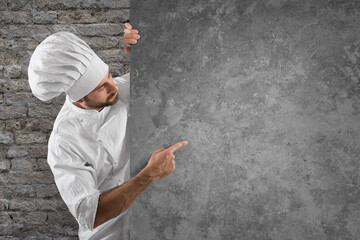 Chef showing and indicates his menu on a grey billboard © Designpics