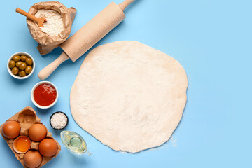 Raw dough and ingredients for preparing vegetable pie on blue background