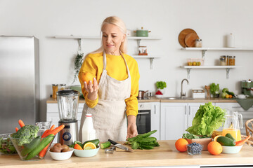 Mature woman with fresh vegetables and fruits making healthy smoothie in kitchen
