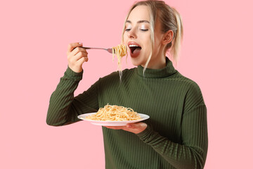 Young woman eating tasty pasta on pink background