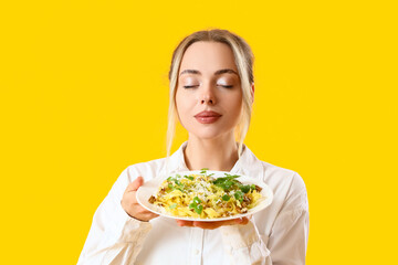 Young woman with tasty pasta on yellow background, closeup