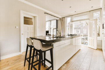 a kitchen with white cabinets and black counter tops on the island in front of the bar stools that is next to the sink
