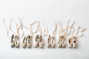 Many pairs of ballet shoes in pairs stand in a row. Pointe shoes in different condition from new to very shabby old. Tapes are accurately laid out in different directions. Studio shooting, horizontal 